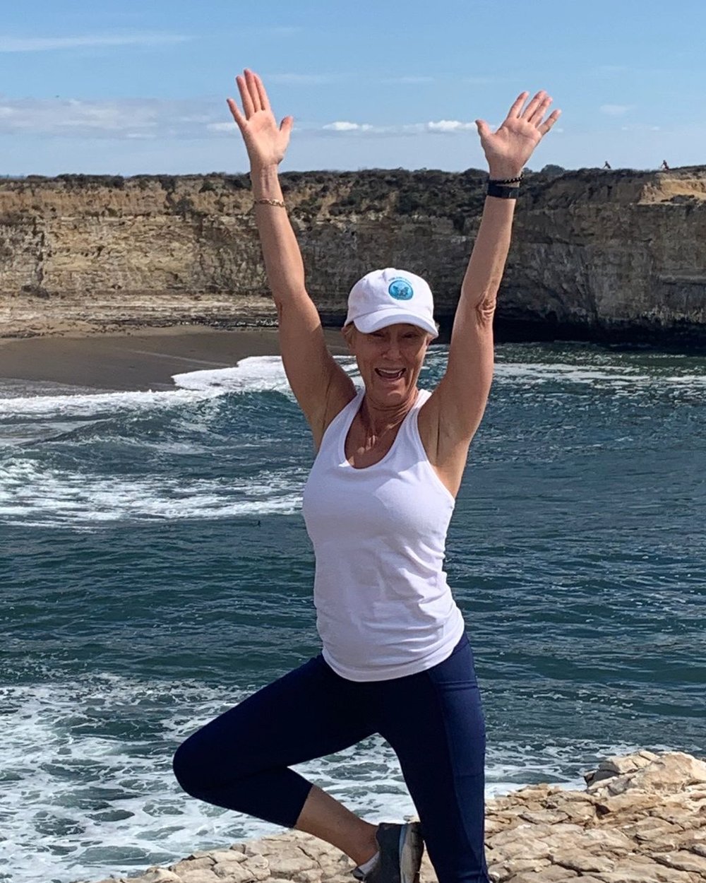 Kristin Kurtz, smiling, arms raised on the California coast